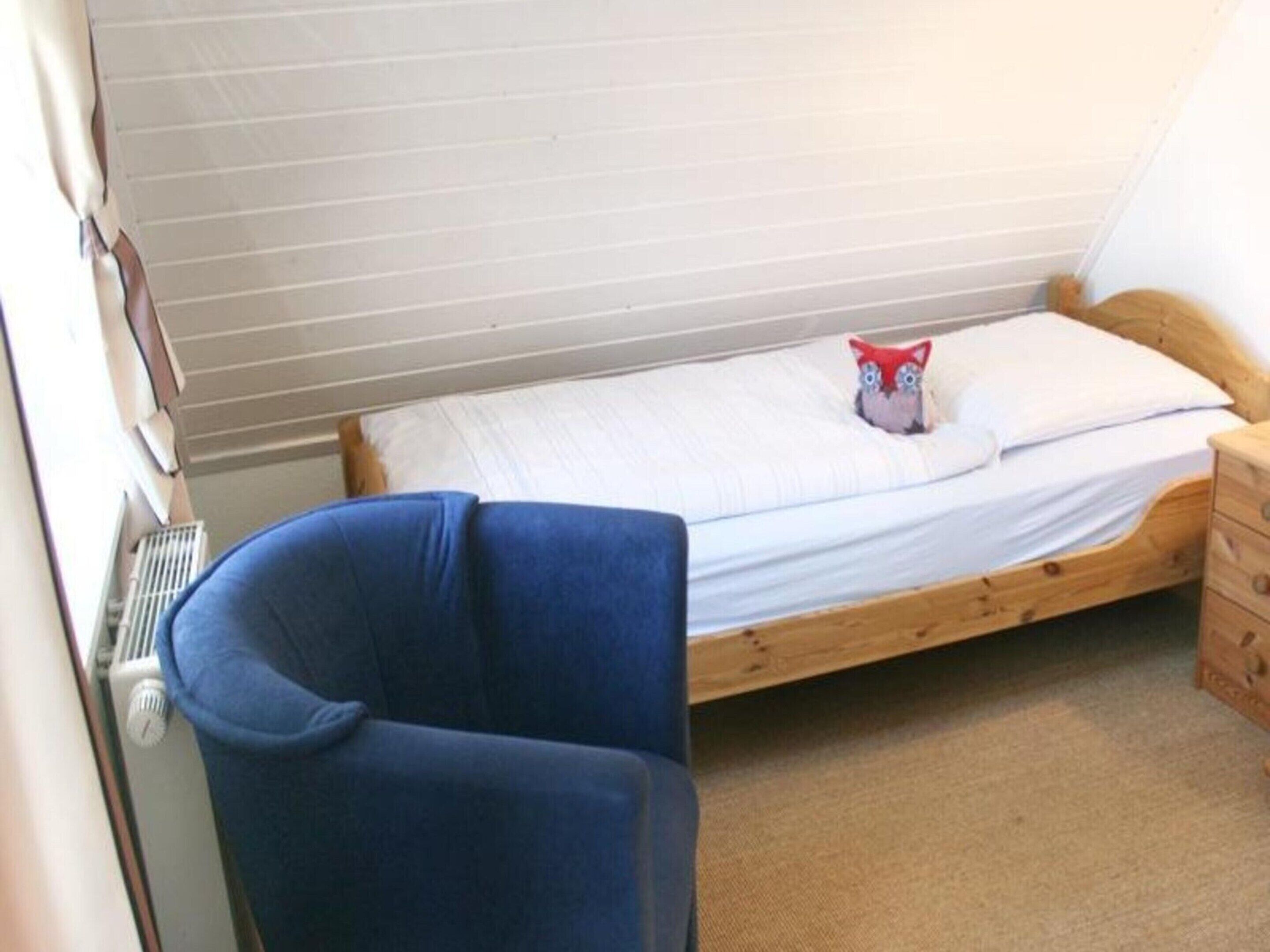 A small, single-bed room with a wooden frame, a blue chair, and a radiator.