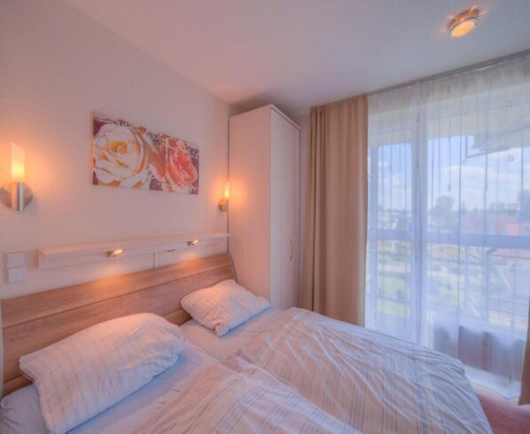 Une chambre d’hôtel avec un grand lit, deux lampes de chevet, un tableau au mur et une vue sur l’extérieur par une fenêtre avec des rideaux.