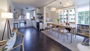 A modern kitchen with dark tiles, a dining area with a wooden table and chairs, and a bookshelf filled with books. - Zeeland Retreat; Sauna and Seaside Charm (Wemeldinge)