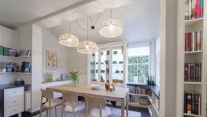 A modern dining area with a wooden table, four chairs, and a vase of tulips. There are bookshelves on both sides of the room, and a window with a view of greenery. - Zeeland Retreat; Sauna and Seaside Charm (Wemeldinge)