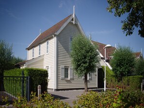 Ett tvåvåningshus med ett brant tak, en veranda och en inhägnad trädgård.