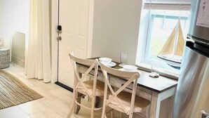 A small, clean room with a wooden table and chairs, a white door, and a window with blinds. - 01 Coastal Cute 2 Bdrm - FLL-DT-Beach (Fort Lauderdale)