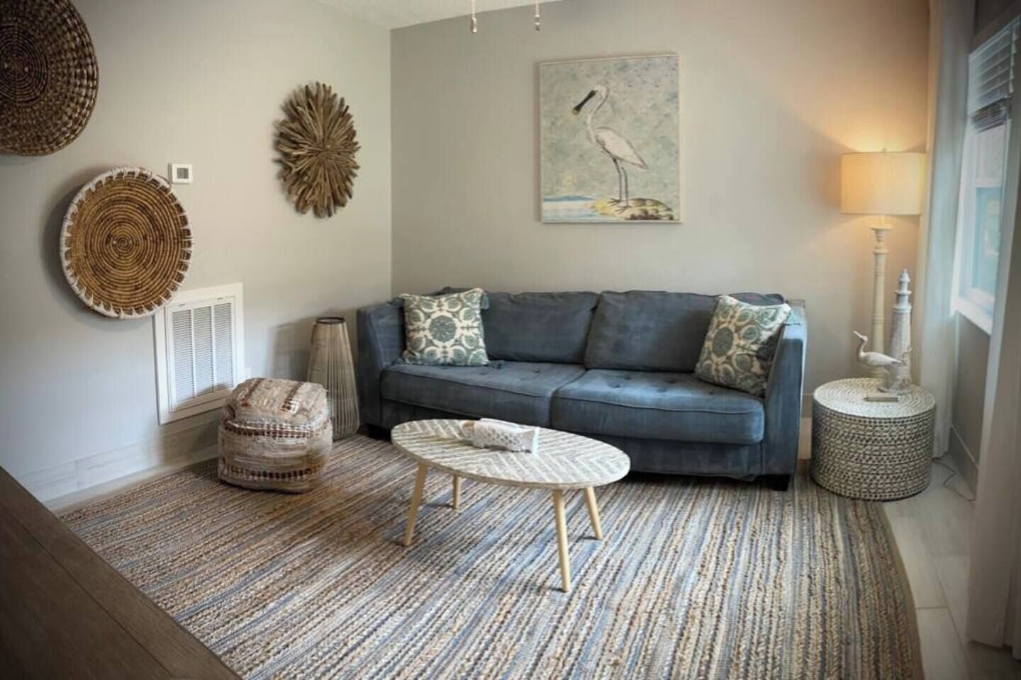 A living room with a grey sofa, patterned cushions, a round coffee table, and a woven rug.