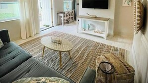 A modern living room with a sofa, coffee table, and a TV on a white console. - 01 Coastal Cute 2 Bdrm - FLL-DT-Beach (Fort Lauderdale)