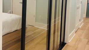 Une chambre d’hôtel moderne dotée d’une porte-fenêtre coulissante donnant sur un balcon, d’un plancher en bois et d’un lit blanc.