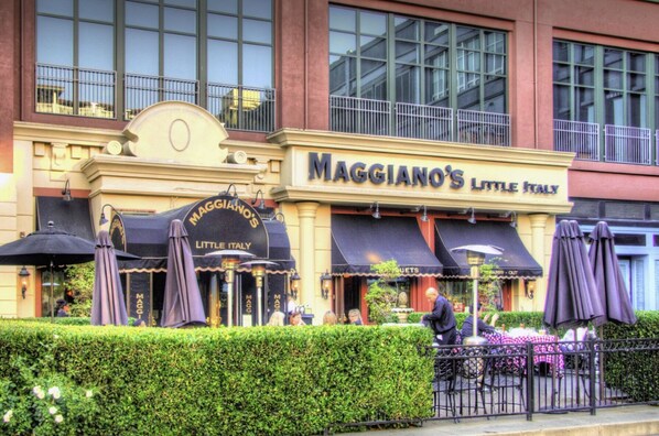 Un edificio con un letrero que dice "MAGGIANO'S LITTLE ITALY" y mesas al aire libre con sombrillas.
