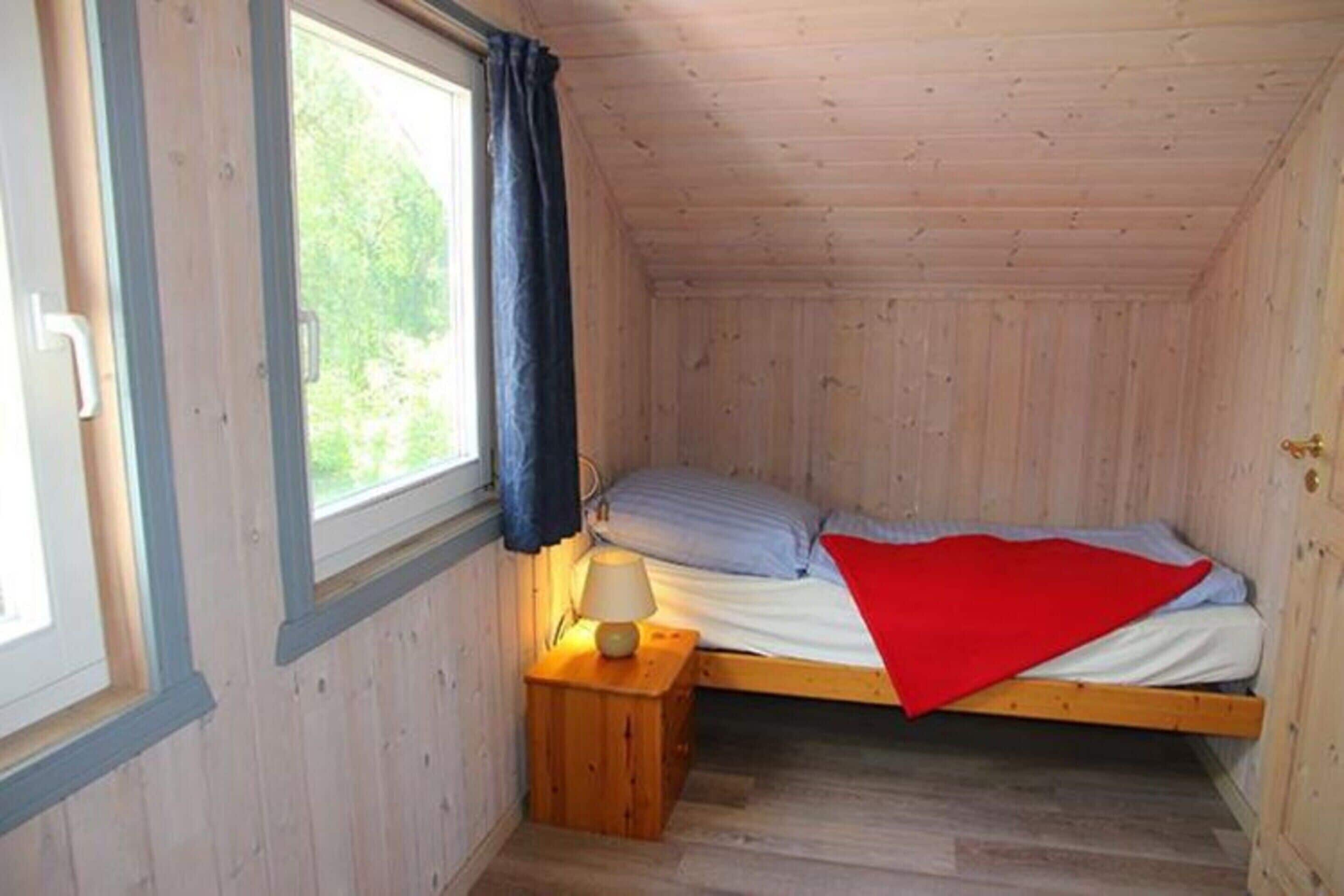 Una habitación pequeña con cama individual, paredes de madera y ventana con cortinas.