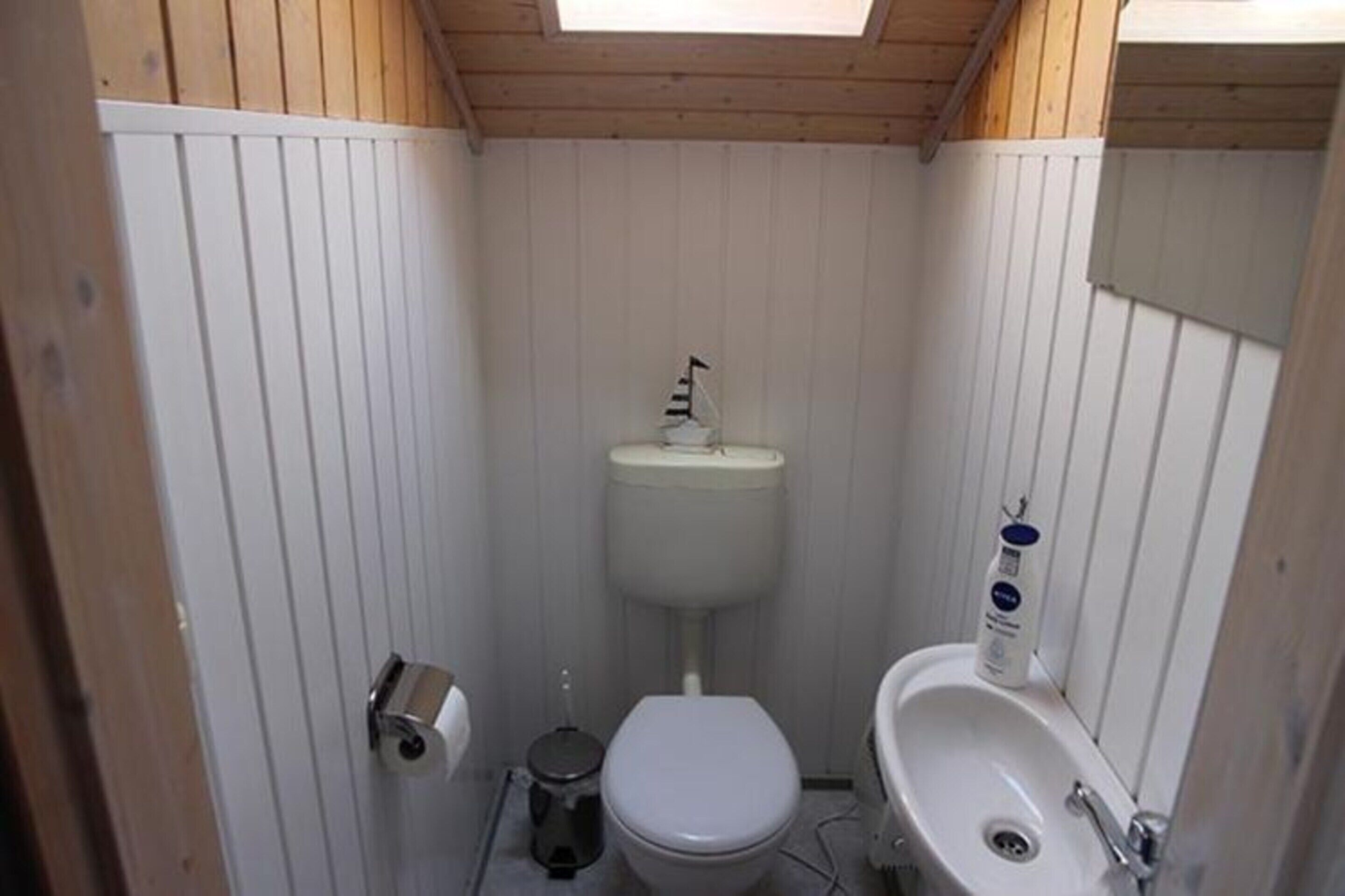 Une petite salle de bain compacte, avec des toilettes, un lavabo et des murs en bois.