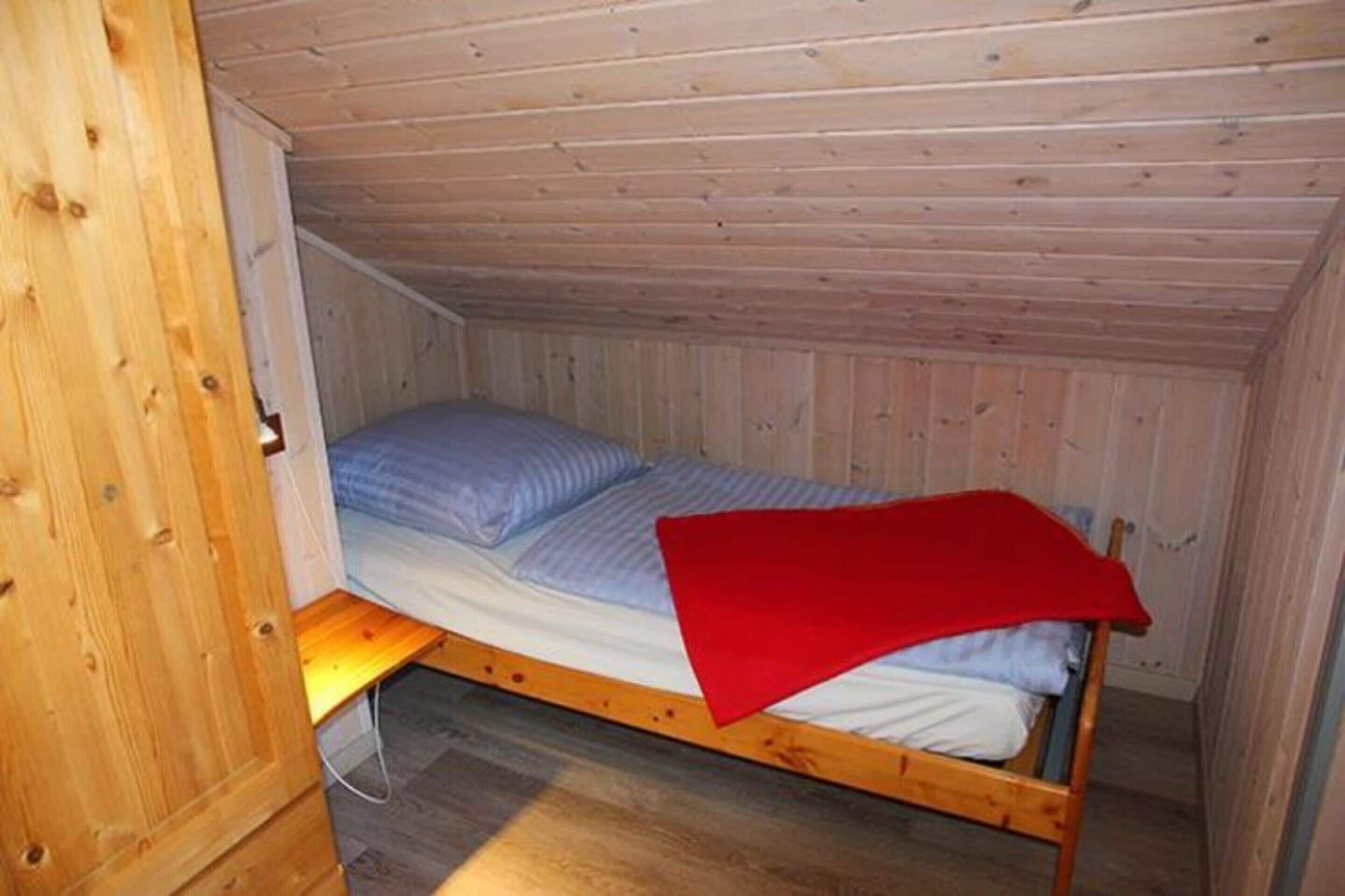 A small, single-bed room with wooden walls and a sloped ceiling.