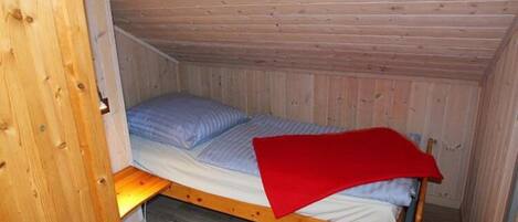 A small, single-bed room with wooden walls and a sloped ceiling.