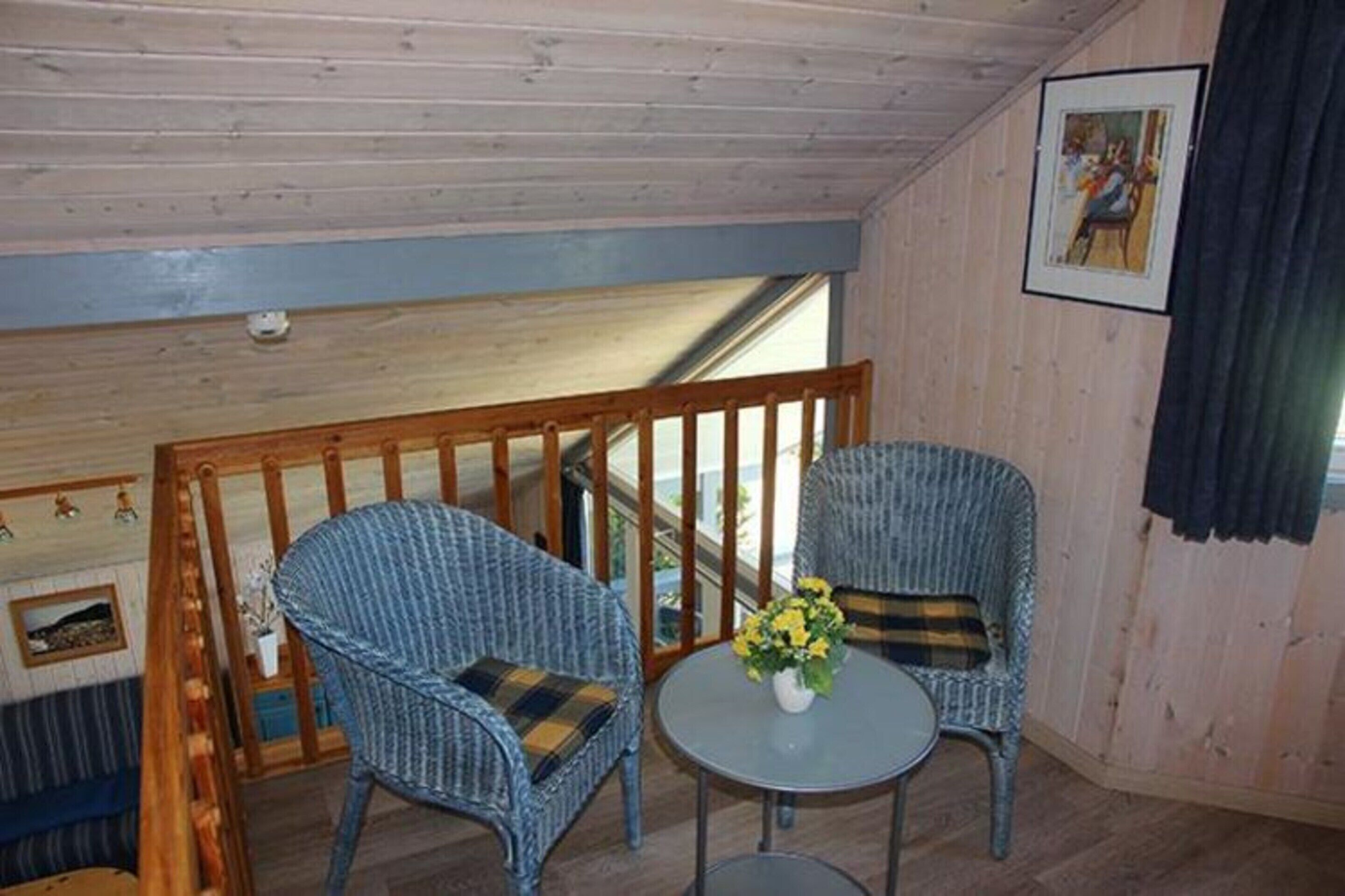 Une pièce comprenant deux fauteuils en osier, une petite table ronde ornée d’un vase de fleurs et une rambarde en bois.