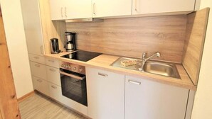 A compact kitchen with white cabinets, a black stove, a sink, and a coffee maker. - Ferienhaus im Ferienpark Mirow (Mirow)