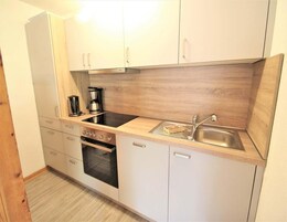 A compact kitchen with white cabinets, a black stove, a sink, and a coffee maker.