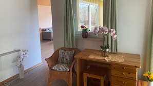 A room with a wooden ceiling, a window with curtains, a wicker chair, a wooden desk, and a radiator. - Ferienhaus im Ferienpark Mirow (Mirow)