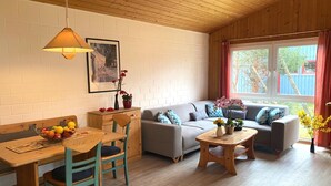 A cozy living room with a wooden ceiling, a sofa set, a dining table with chairs, and a window with curtains. - Ferienhaus im Ferienpark Mirow (Mirow)