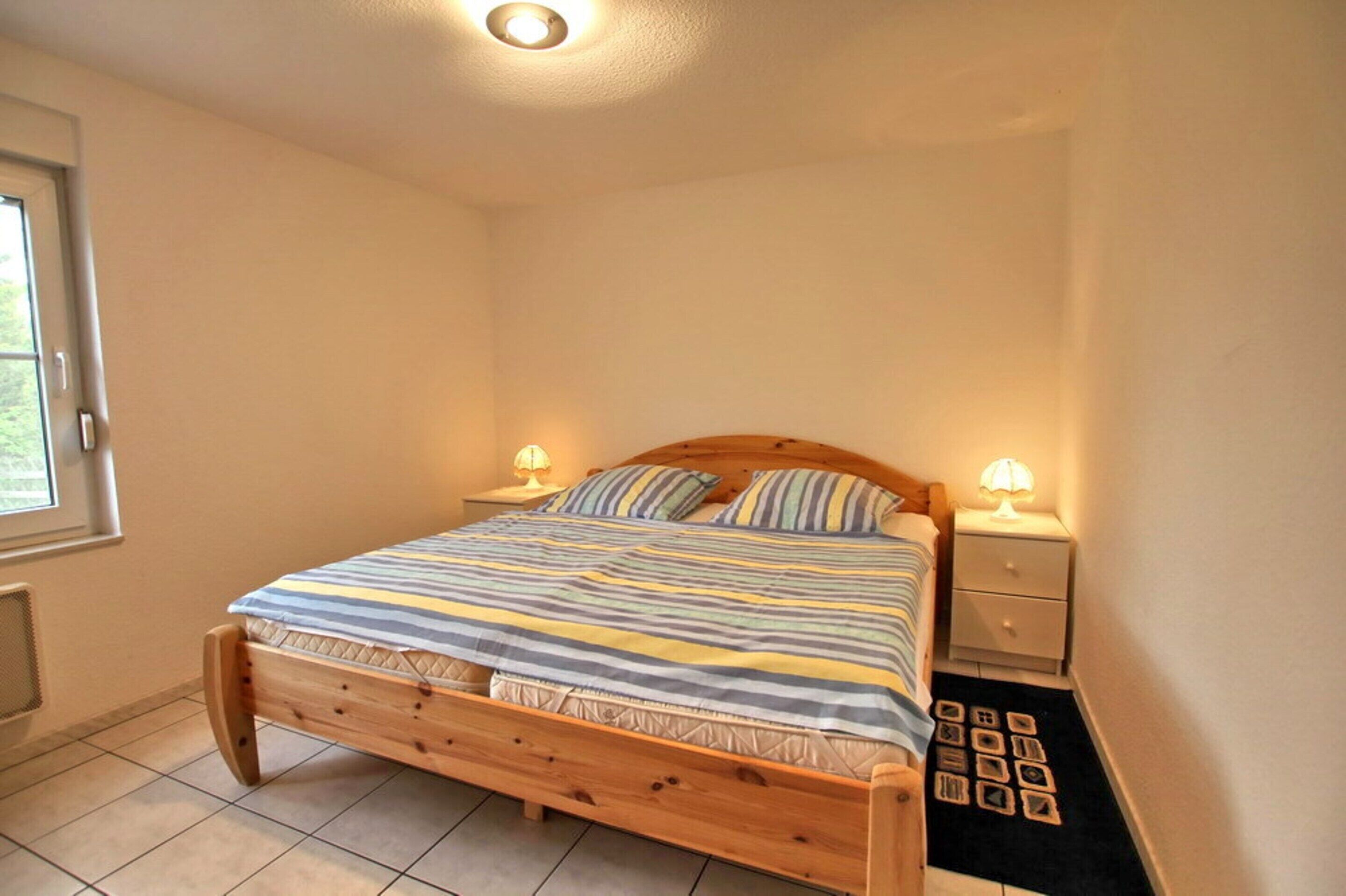 Ein Schlafzimmer mit einem hölzernen Bett, zwei Nachttischen mit Lampen, einem Fenster und einer Heizung.