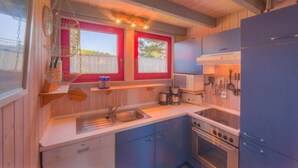 A compact kitchen with wooden cabinets, a sink, a stove, and a refrigerator. - Ferienhaus im Ferienpark Mirow (Mirow)