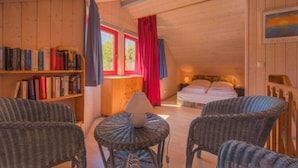 A cozy room with a wooden ceiling, a bed, a bookshelf, and wicker chairs. - Ferienhaus im Ferienpark Mirow (Mirow)