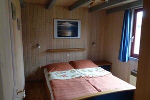 A wooden-paneled room with a bed, a small table, and a window with curtains.