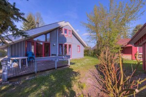A two-story house with a wooden deck, a small outdoor seating area, and a red barn in the background.