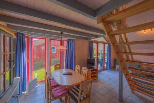 Una habitación con una mesa y sillas de madera, un televisor y una escalera.