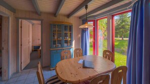 A wooden dining area with a table and chairs, a blue cabinet, and a view of a garden through large windows. - Gemutliches Ferienhaus im Skandinavischen Stil (Mirow)