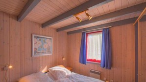 A wooden-paneled room with a bed, a nightstand, a wall-mounted lamp, and a window with curtains. - Gemutliches Ferienhaus im Skandinavischen Stil (Mirow)
