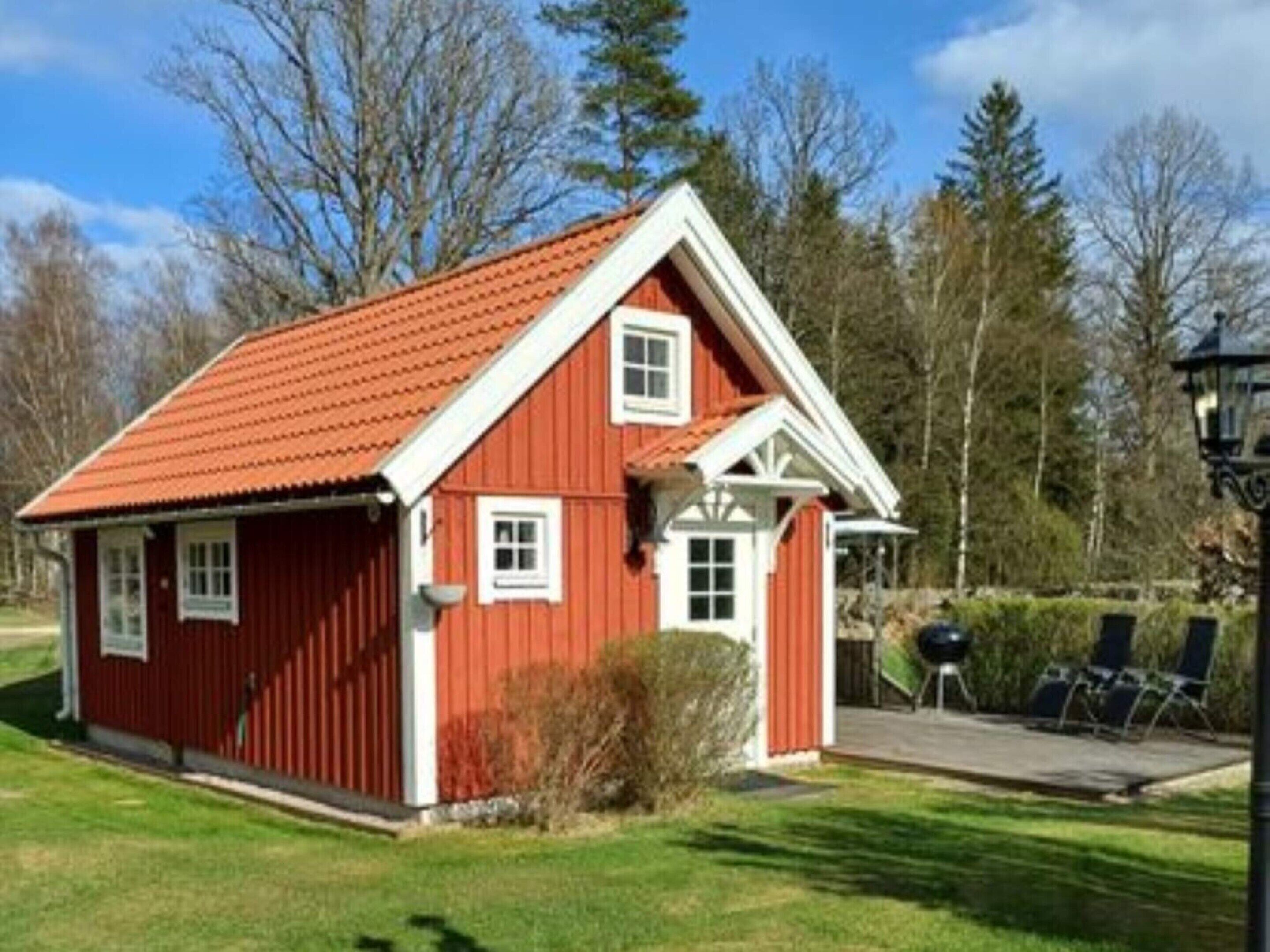 A red wooden house with a gabled roof, a small porch, and a lawn.
