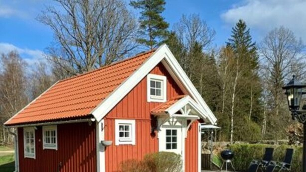 Ein rotes Holzhaus mit Satteldach, einer kleinen Veranda und einem Rasen.
