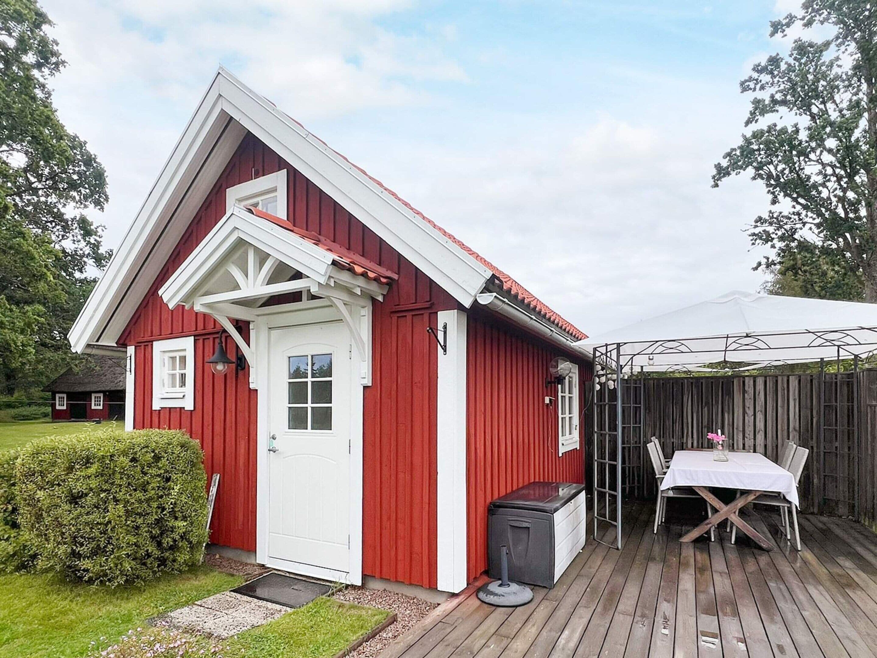 A red wooden building with a white door and windows, a small porch, and a table with chairs outside.