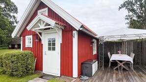 A red wooden building with a white door and windows, a small porch, and a table with chairs outside. - 5 Person Holiday Home in Linneryd (Linneryd)