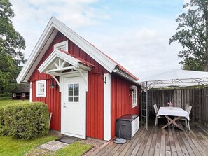 A red wooden building with a white door and windows, a small porch, and a table with chairs outside. - 5 Person Holiday Home in Linneryd (Linneryd)