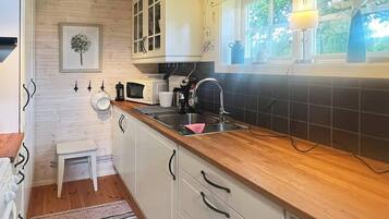 A compact kitchen with white cabinets, a wooden countertop, a sink, a microwave, and a window with a view of greenery.