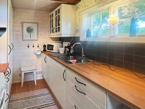 A compact kitchen with white cabinets, a wooden countertop, a sink, a microwave, and a window with a view of greenery. - 5 Person Holiday Home in Linneryd (Linneryd)
