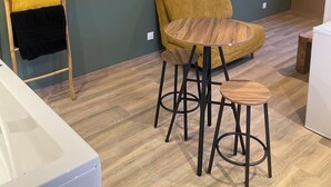 Een kamer met een houten tafel en twee krukken, een aan de muur bevestigde televisie en een houten ladder met handdoeken.