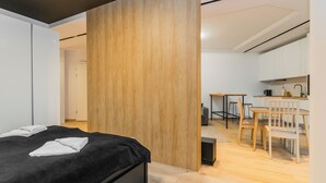 A modern bedroom with a bed, a wooden column, and a kitchenette area with a dining table and chairs.