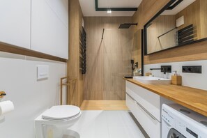Ett modernt badrum med ett tvättställ i trä, en handfat, en toalett och en tvättmaskin.