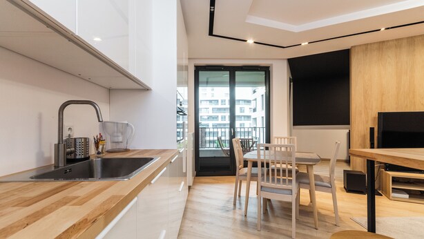 A modern kitchen with a wooden countertop, stainless steel sink, and a dining area with a table and chairs.