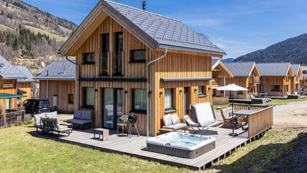 A wooden lodge with a hot tub and outdoor seating on a deck. - Chalet With Spacious Terrace (Sankt Georgen am Kreischberg)