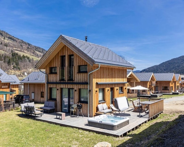 A wooden lodge with a hot tub and outdoor seating on a deck.