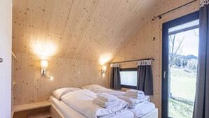 A wooden cabin bedroom with a bed, two wall-mounted lights, a window with curtains, and a view of the outdoors. - Chalet With Spacious Terrace (Sankt Georgen am Kreischberg)
