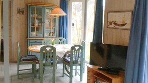 Un coin repas comprenant une table et des chaises, un téléviseur et un meuble avec des portes en verre.