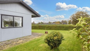 Ett modernt hus med en grå fasad, ett stort fönster och en välskött gräsmatta med en liten buske och en krukväxt.