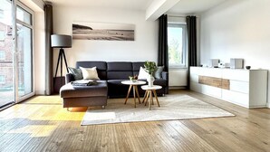 A modern living room with a dark sofa, a small round table, and a lamp. - Ferienwohnung Sturmeck, Fehmarn-orth (Fehmarn)