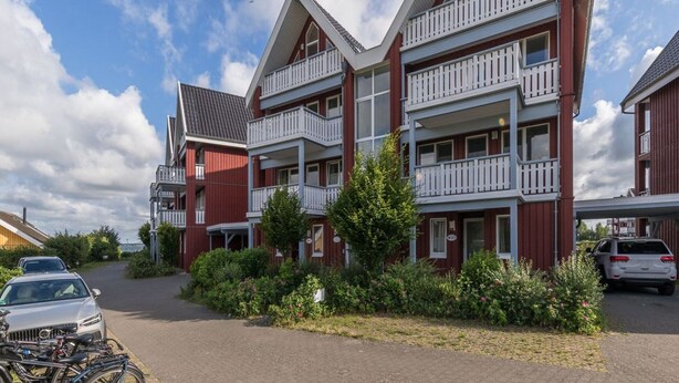 A multi-story building with balconies, a paved driveway, and parked cars. - Appartement im Ferienpark in Rechlin (Rechlin)