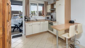 A modern kitchen with white cabinets, a wooden dining table, and a bar stool. - Appartement im Ferienpark in Rechlin (Rechlin)