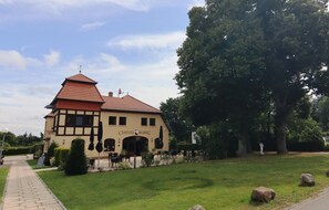 A building with a sign reading "CHEVAL BLANC" and a red roof, surrounded by a grassy area with trees and a pathway. - Exklusives Ferienhaus Oliver mit Sauna in Wendorf (Kuhlen-Wendorf)