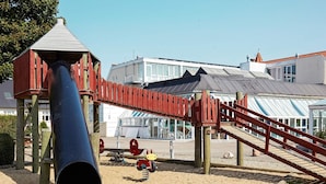 A playground with a slide and climbing structures, a wooden bridge, and a building with a sloped roof in the background. - 6 Person Holiday Home on a Holiday Park in Hejls (Hejls)