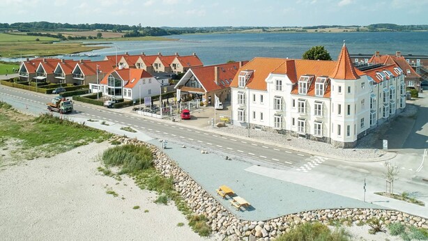 A large white building with red roofs, situated by a road with a view of a lake. - 6 Person Holiday Home on a Holiday Park in Hejls (Hejls)