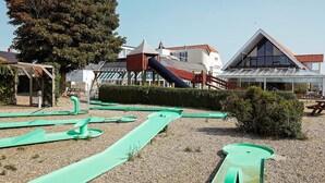 A playground with slides and a climbing structure, surrounded by buildings and a large tree. - 4 Person Holiday Home on a Holiday Park in Hejls (Hejls)